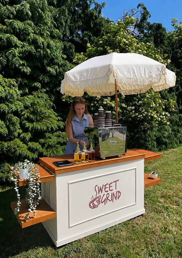 Abbie West preparing drinks at the Sweet Grind mobile coffee cart under a fringed parasol