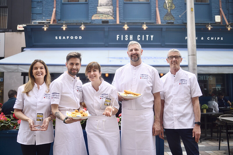 Five Fish City chefs in whites outside the restaurant holding dishes of fish and chips