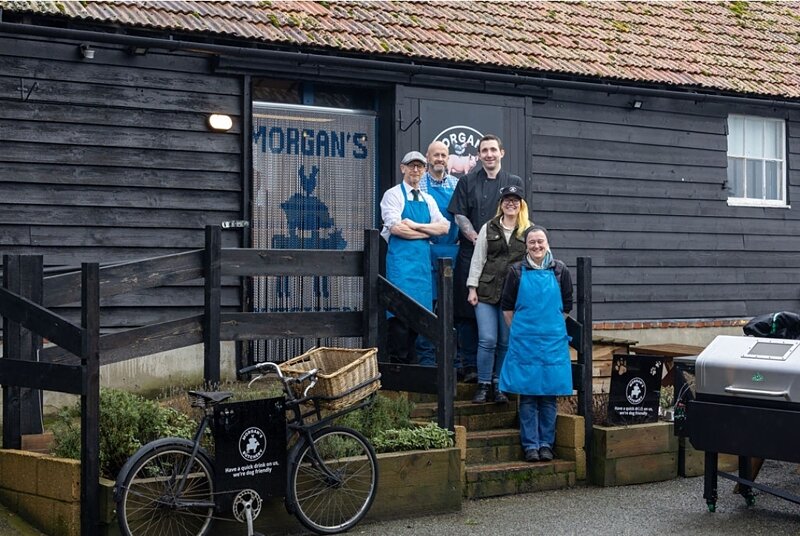 Four staff in aprons on the steps of Morgan's black timber butchery, with a delivery bicycle in front